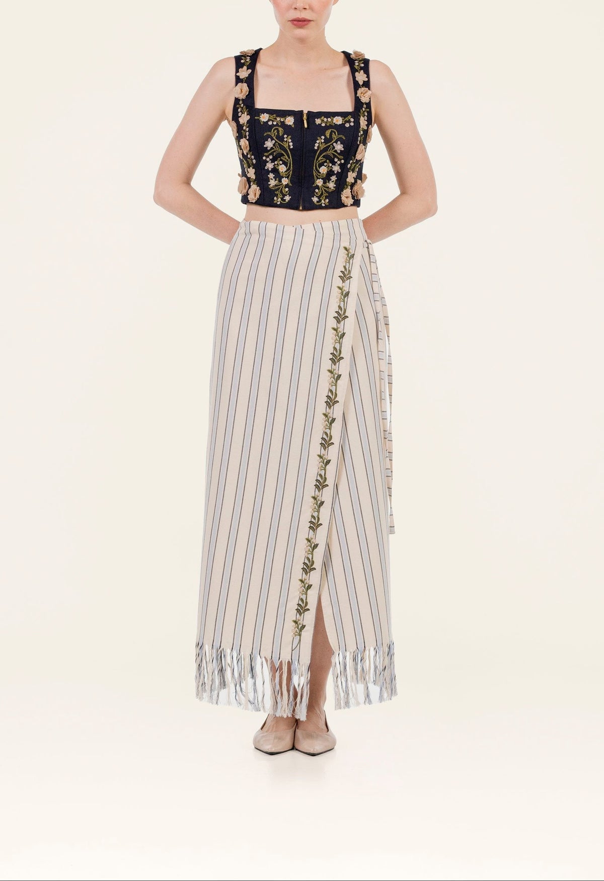 Front view of Maria Valle Pareo skirt showing vertical stripes, embroidered vine trim and fringed hem on pale background