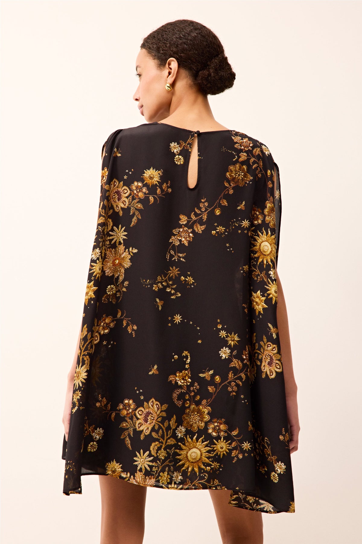 Black short dress with long cape sleeves, a cinched waist, and an allover gold floral pattern.