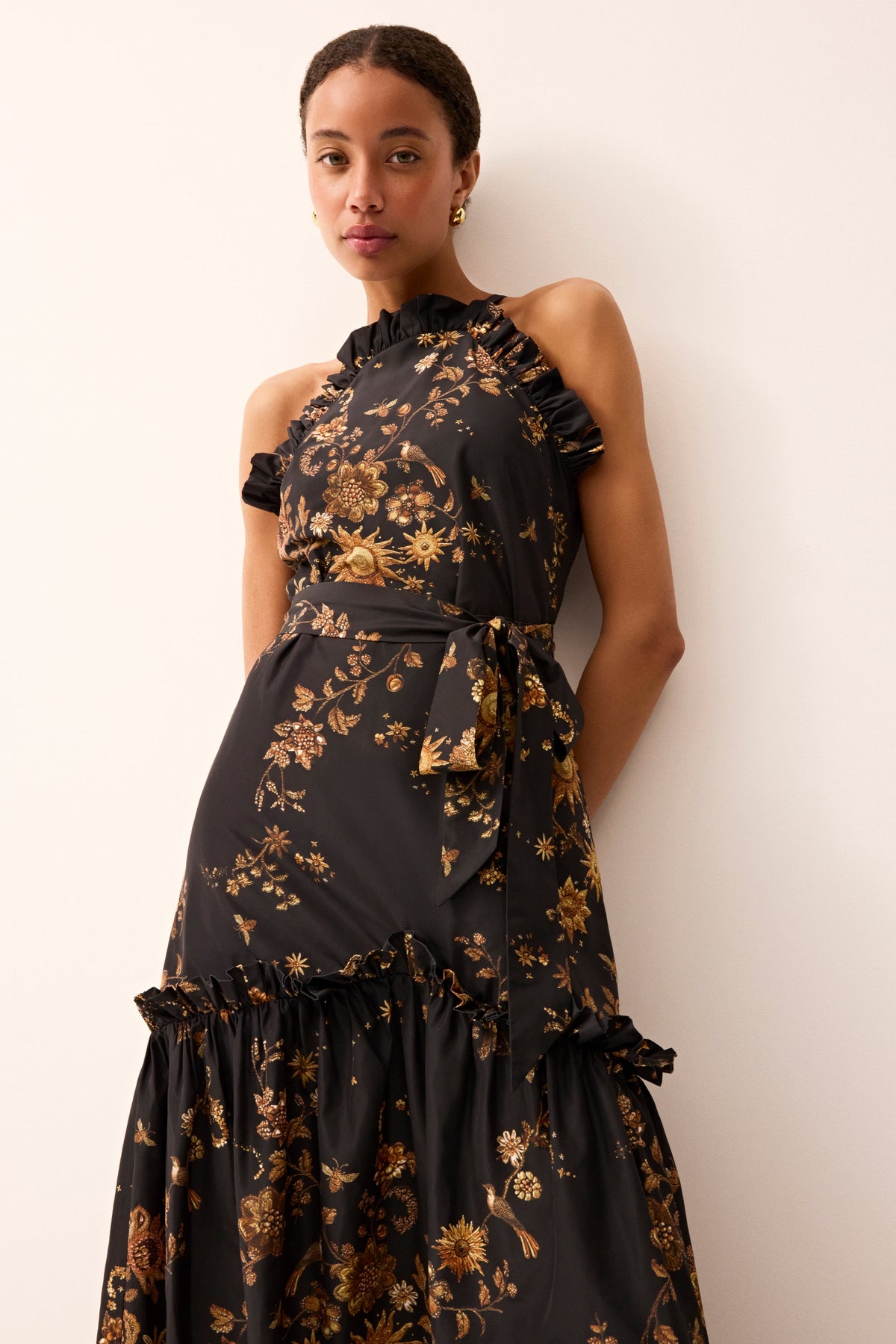 Elegant long halter dress featuring a ruffle-accented skirt and a black and gold floral design throughout.