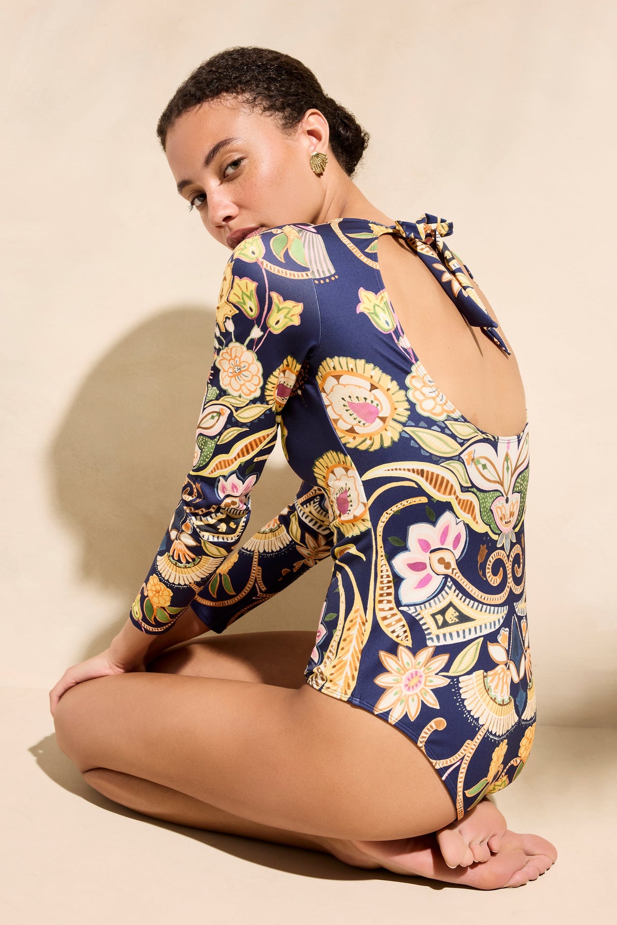 Rear three quarter view of Robin Rashguard in Neptune showing open tie back, long sleeves, floral navy print on beige