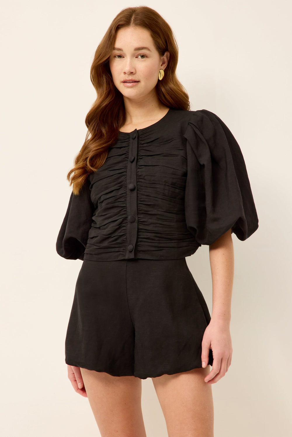 Front view of Rowan Top in black worn by model, showcasing ruched button-front bodice and puff sleeves on light background