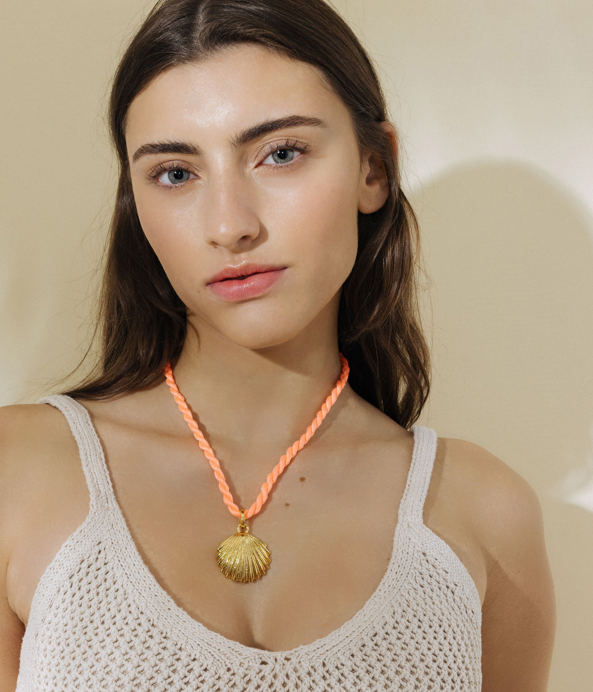 Front view of De La Mer Pendant showcasing its 24K gold finish and shell shape on an orange cord against a white top