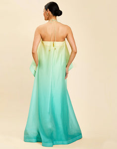 Woman wearing the Mestiza Mariposa Convertible Gown in Tuscan Sunrise print, featuring a column silhouette, removable cape overlay, racerback neckline, open back, self-tie halter straps, and linen organza fabrication.