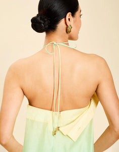 Woman wearing the Mestiza Mariposa Convertible Gown in Tuscan Sunrise print, featuring a column silhouette, removable cape overlay, racerback neckline, open back, self-tie halter straps, and linen organza fabrication.