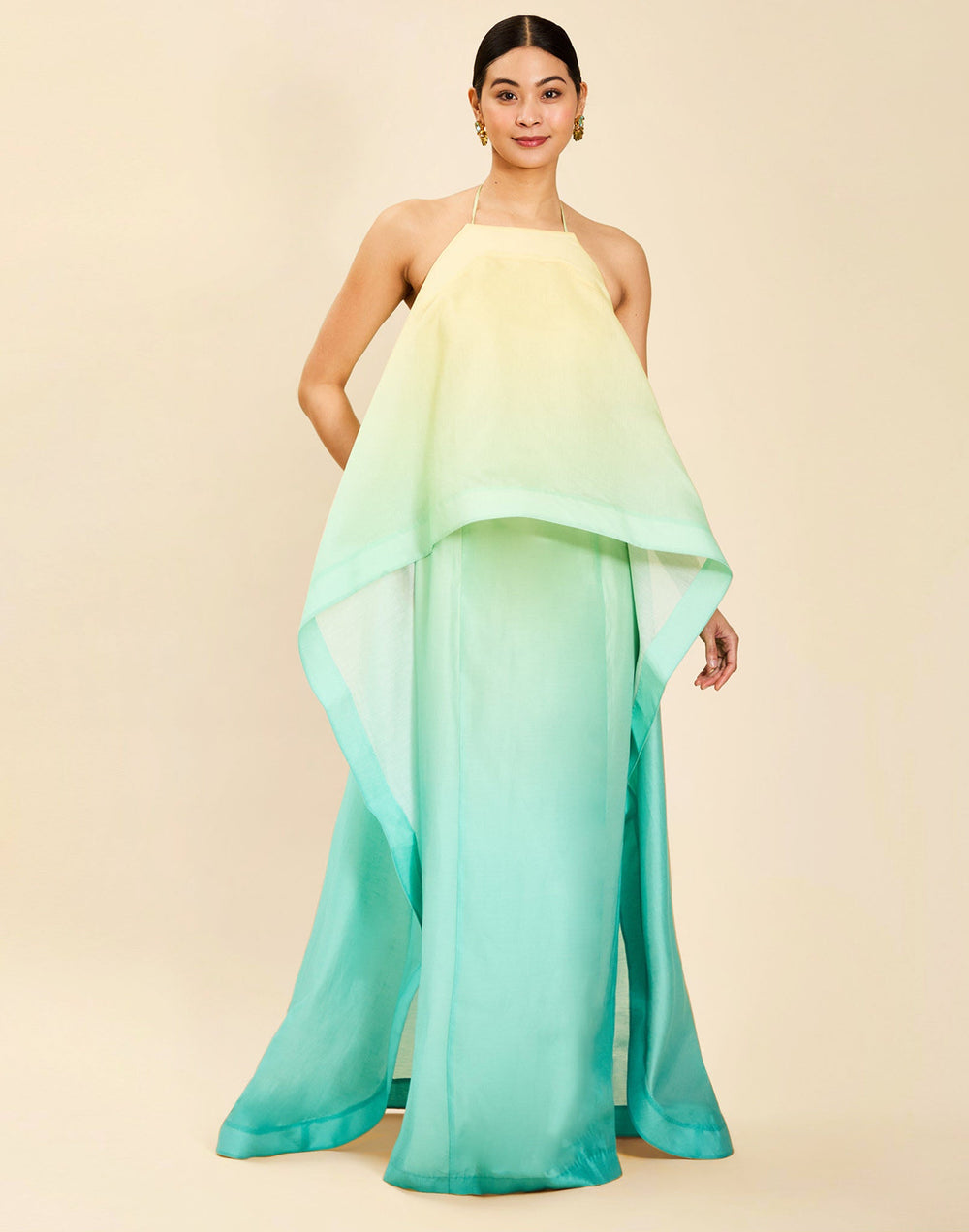Woman wearing the Mestiza Mariposa Convertible Gown in Tuscan Sunrise print, featuring a column silhouette, removable cape overlay, racerback neckline, open back, self-tie halter straps, and linen organza fabrication.