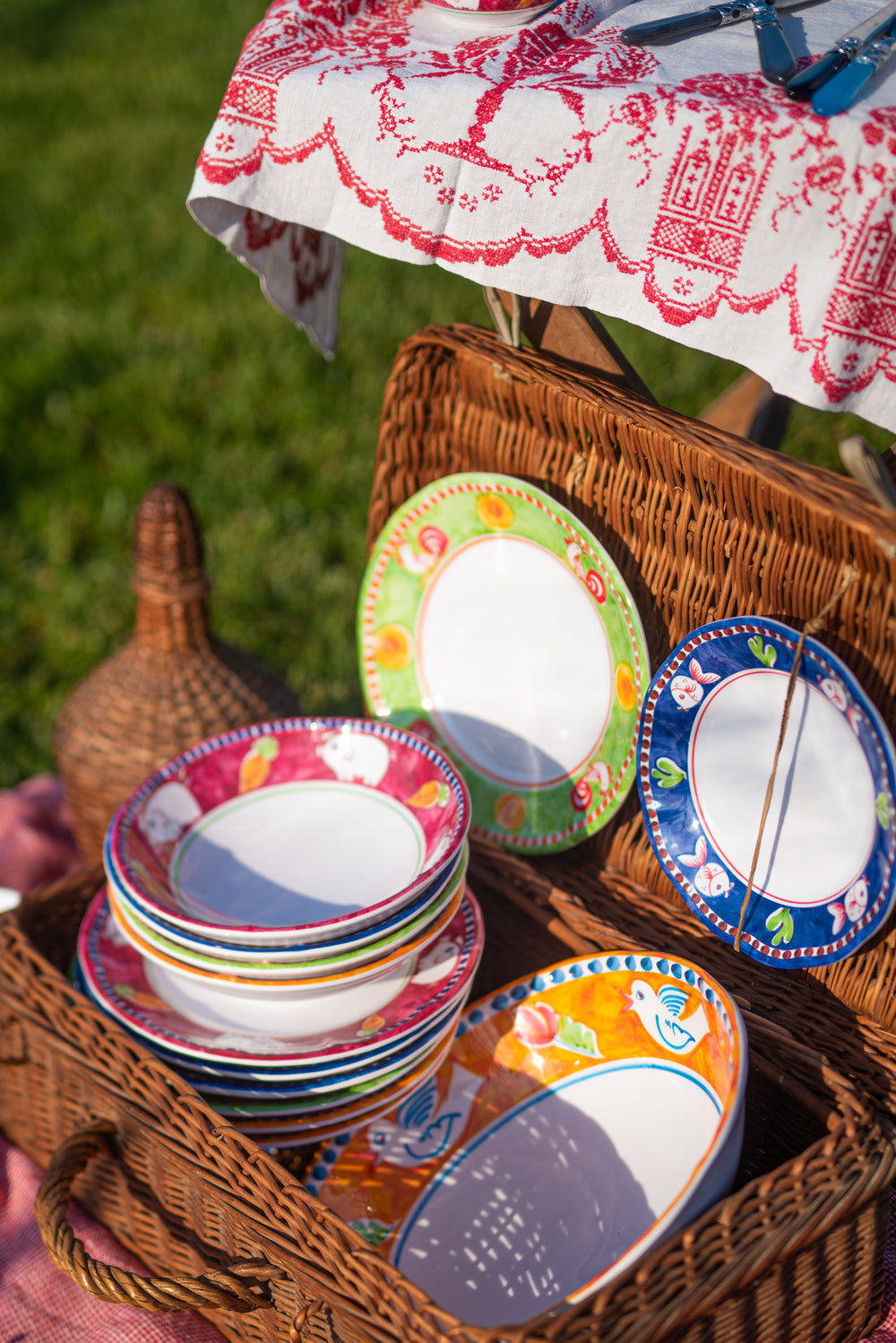 Angled view of Melamine Campagna large serving bowl with orange bird-and-fruit pattern in wicker picnic basket with matching plates