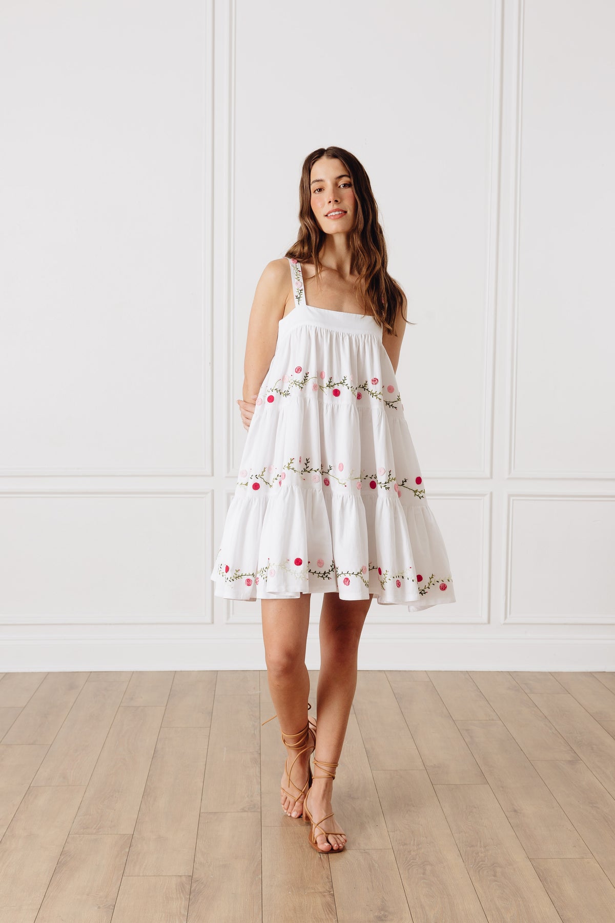 Front view of OTM Exclusive Lila Short Dress showing white tiered body and pink and green floral embroidery on model