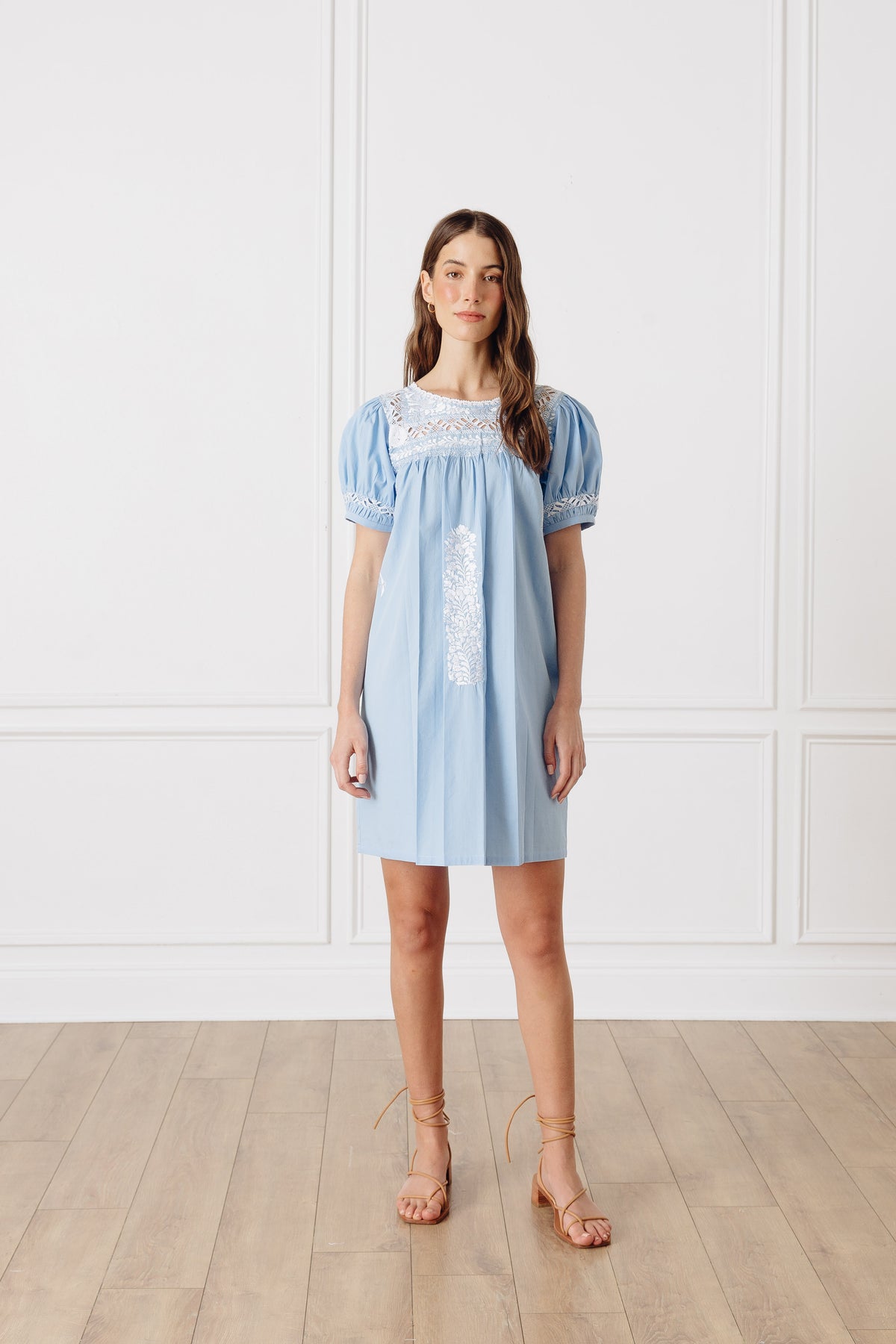 Front view of OTM Exclusive Maria Short Dress showcasing blue cotton, hand pulled lace, and puff sleeves against a white wall