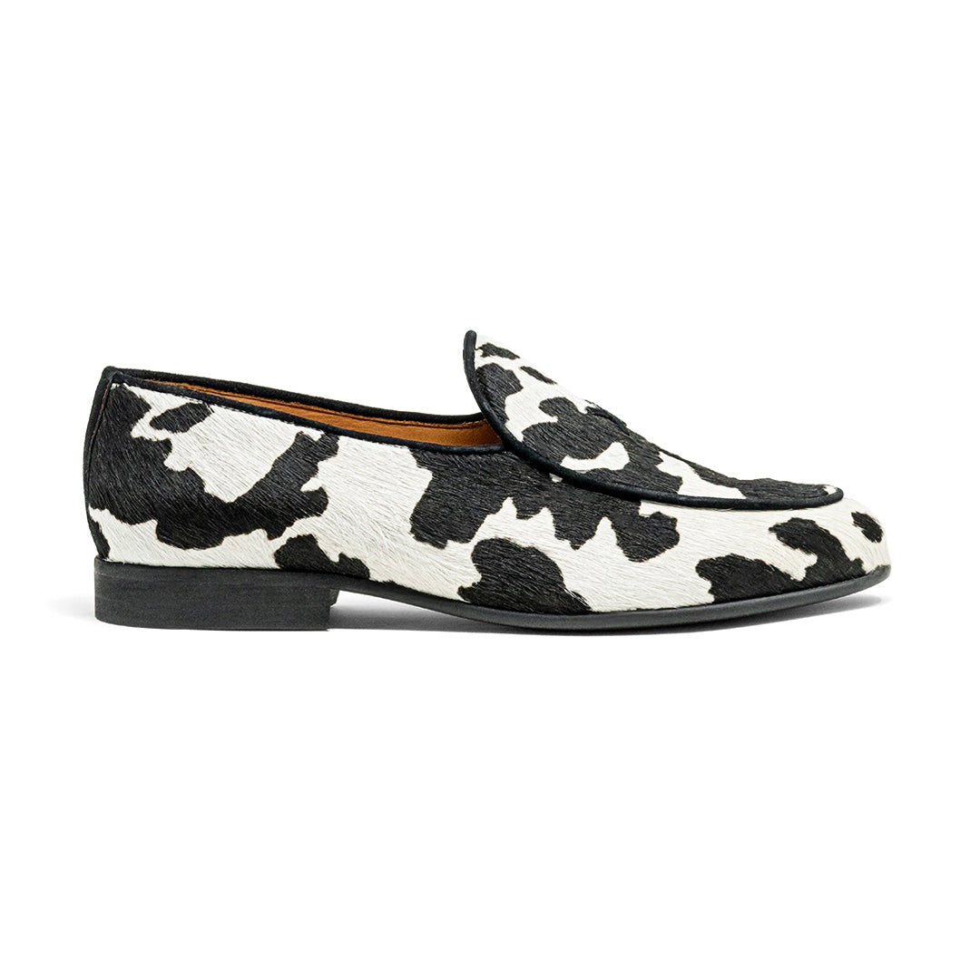 Side view of womens cow print Milano loafer showcasing black and white patterned upper and black rubber sole on white background