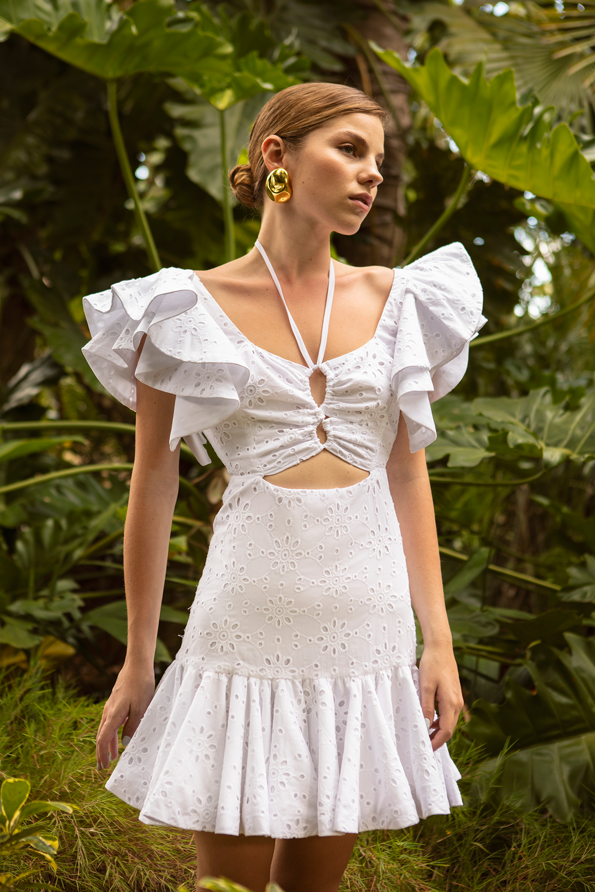 Front view of white eyelet Mini Chocolate dress on model with ruffled puff sleeves, front cutouts and flared hem in leafy setting