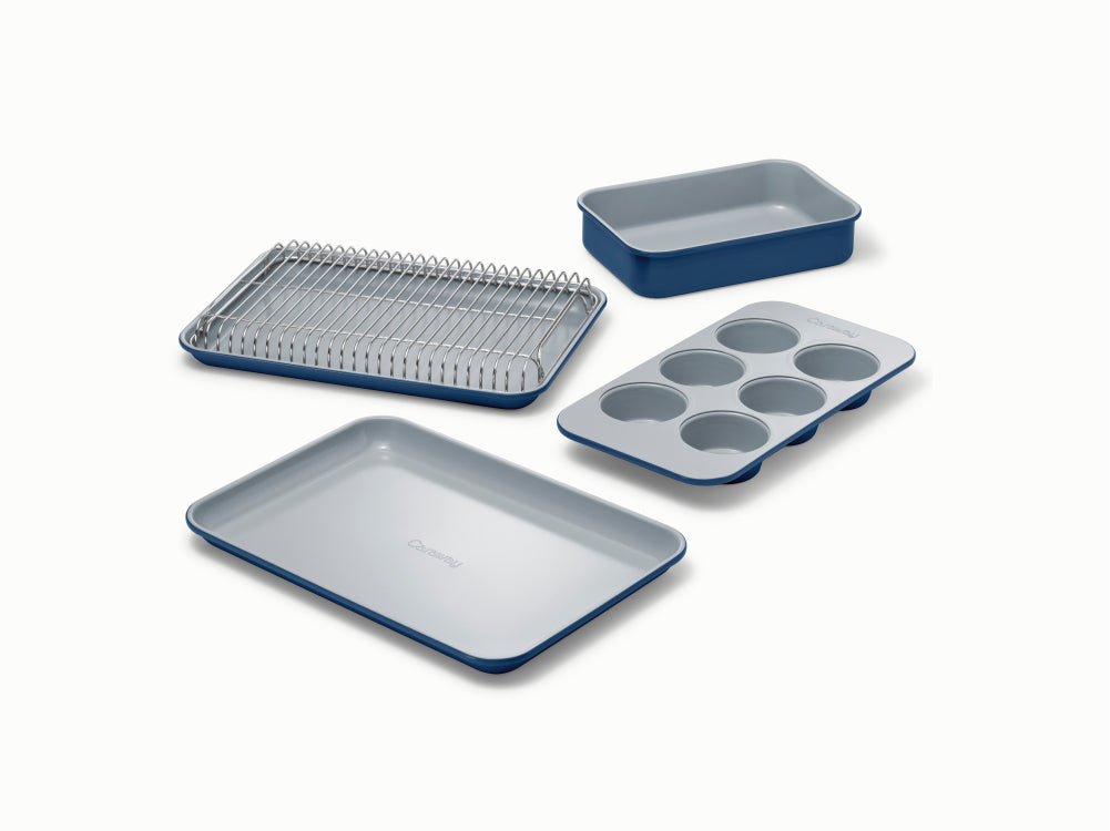Angled view of navy mini bakeware set with 6-cup muffin pan, rimmed baking sheet, loaf pan, and cooling rack on white background