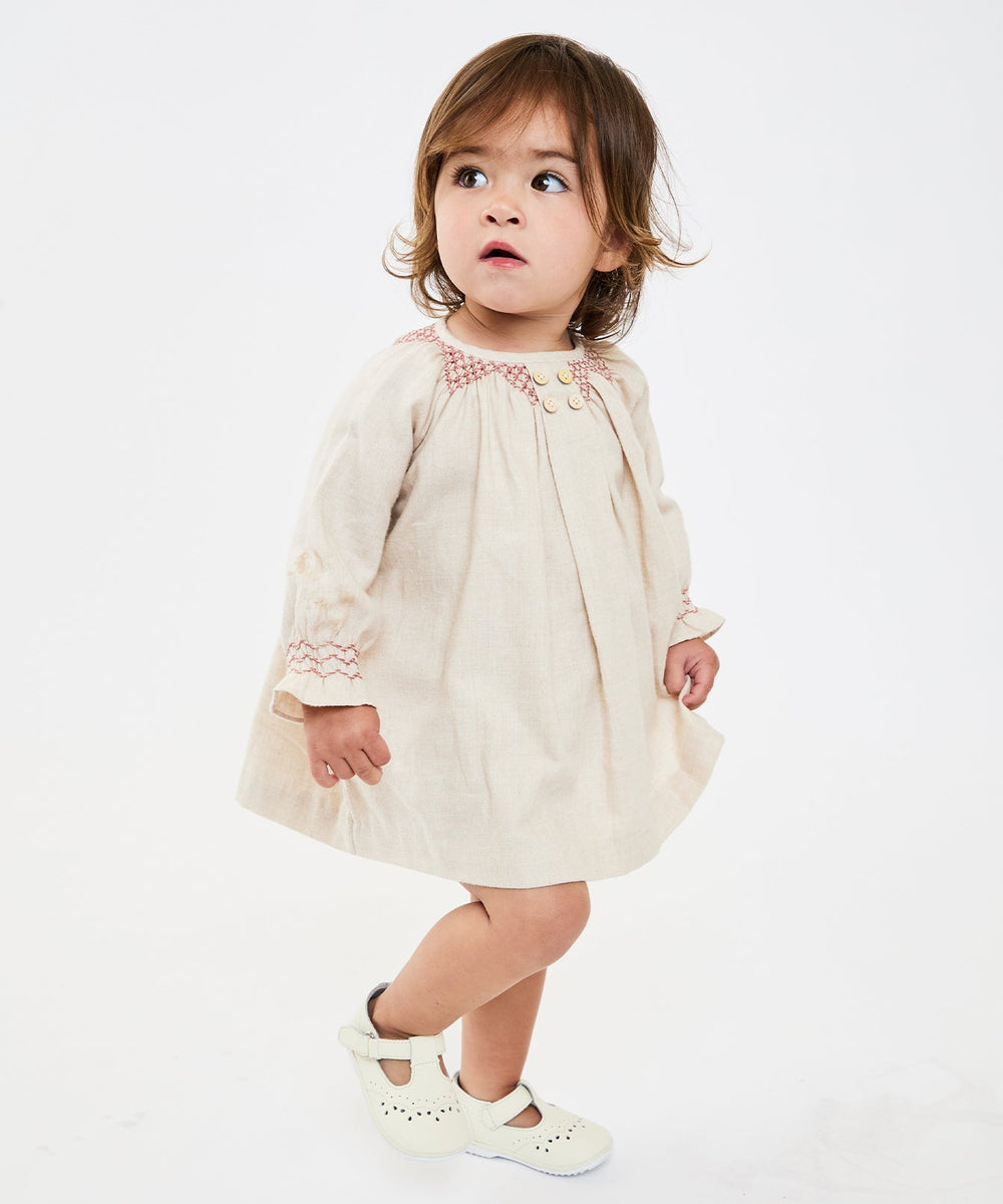 Three-quarter view of Willa baby dress in Rose with hand-smocked neckline, front buttons, and long sleeves