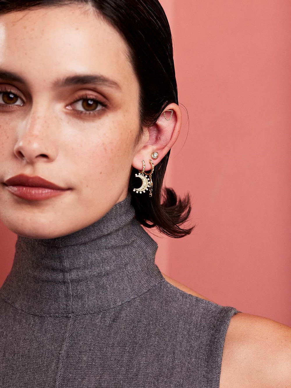 Close-up of model wearing Small Southwestern Moon Earrings showing 14k yellow gold crescent moon with diamond accents on pink background