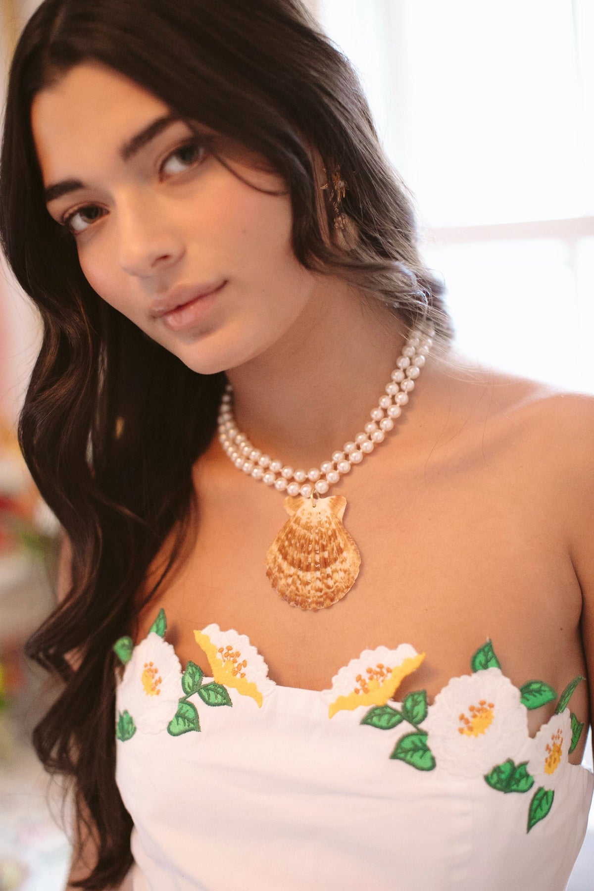 Front close-up of Monaco Necklace on model showing double-strand knotted glass pearls and a neutral shell pendant against soft window light