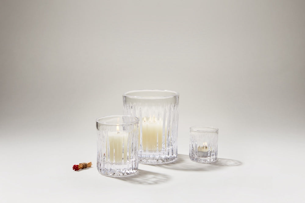 Three Montpelier hurricane glass candle holders with fluted vertical ribbing and ivory pillar candles on a neutral background