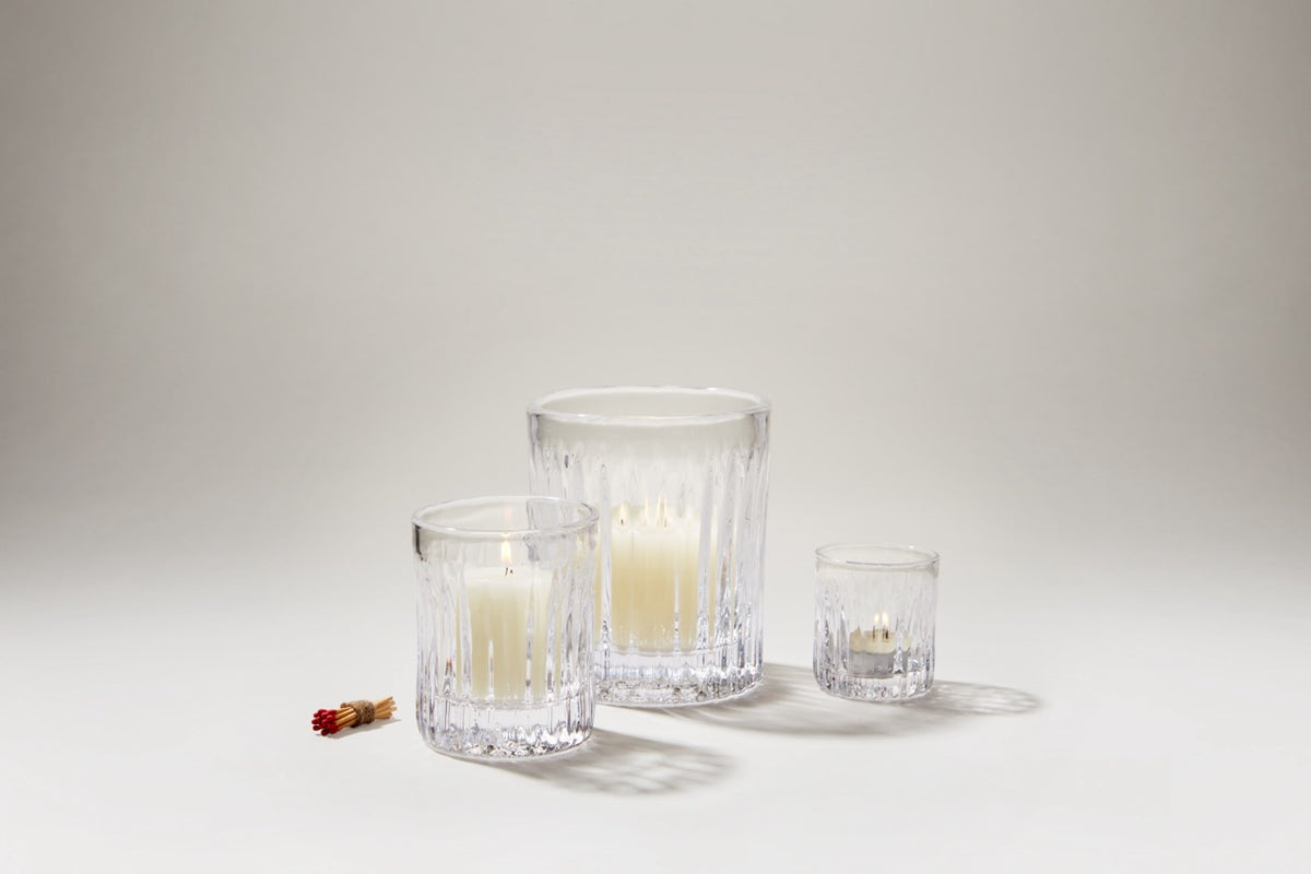 Three Montpelier hurricane glass candle holders with fluted vertical ribbing and ivory pillar candles on a neutral background