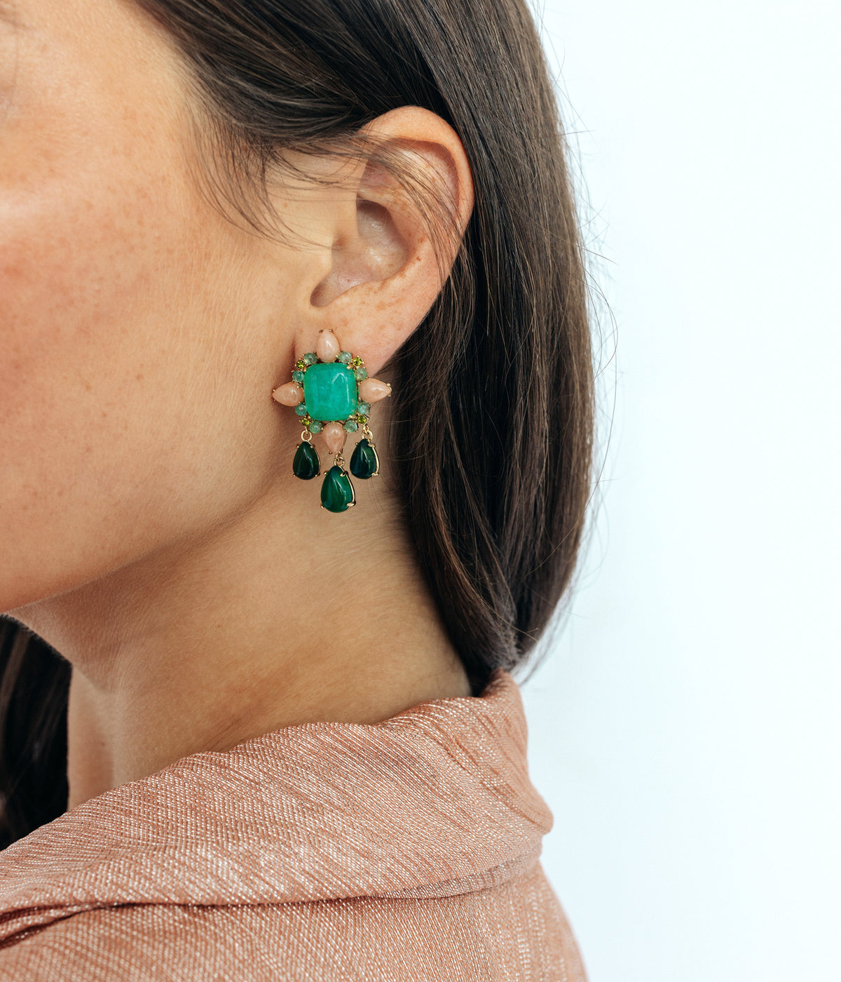 Side view of Montrose Earrings worn on an ear, showcasing dangling green stones and gold-tone finish against a light background