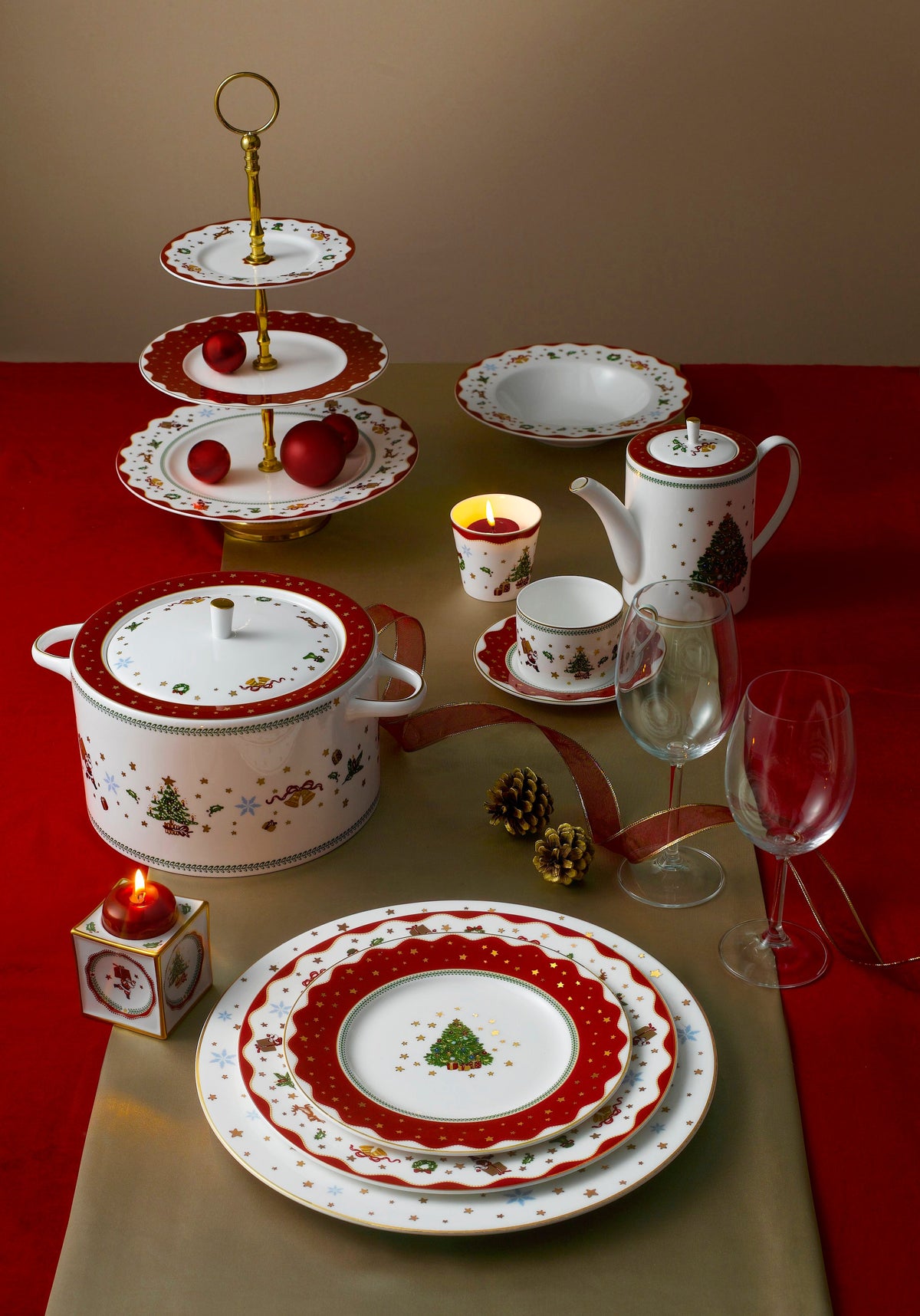 Three-tier My Noel cake stand on a holiday table with matching red-and-gold bone china, candles, and glassware