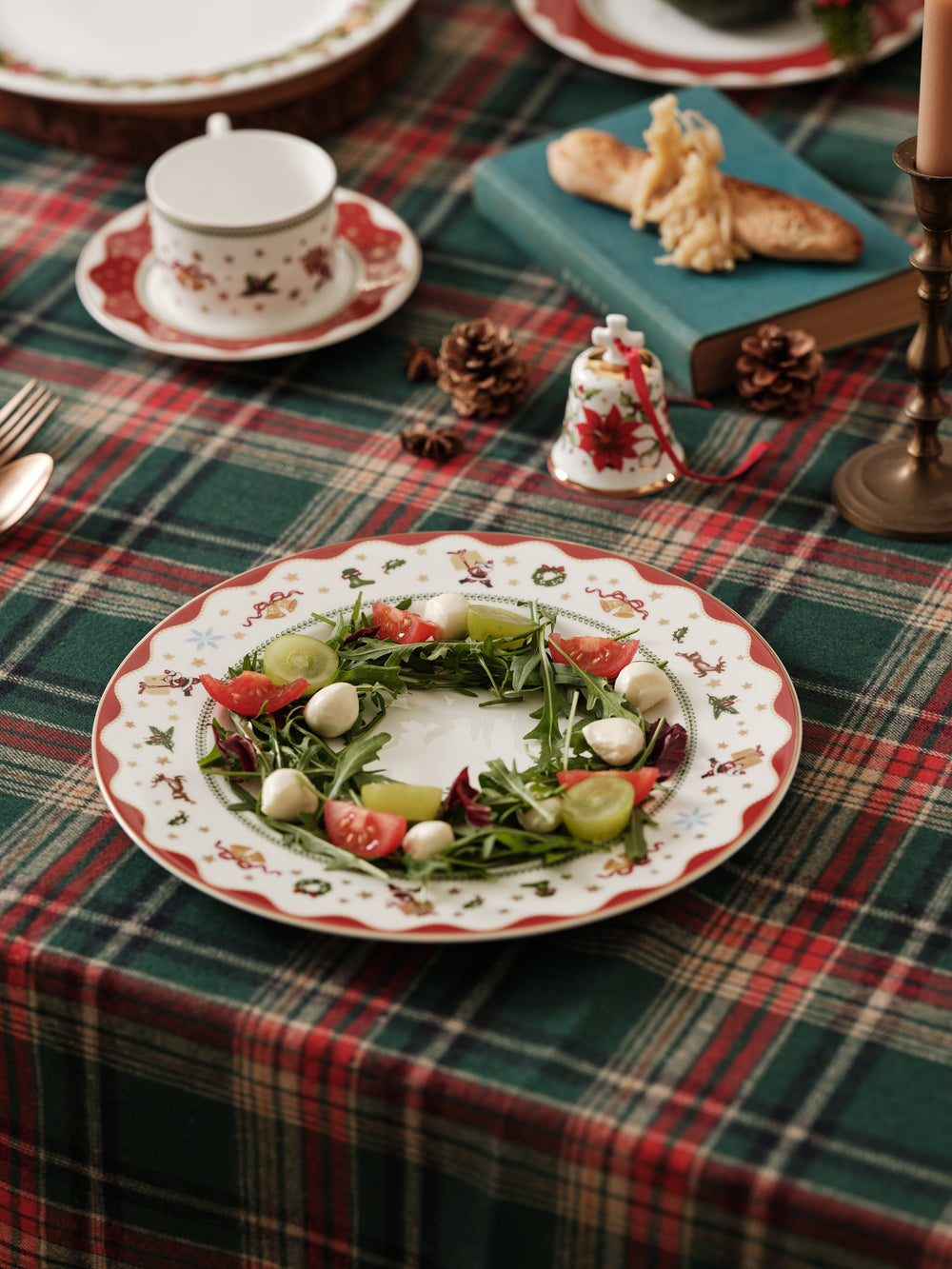 Angled overhead view of My Noel dinner plate showing red scalloped rim with holiday motifs and salad wreath on green plaid tablecloth