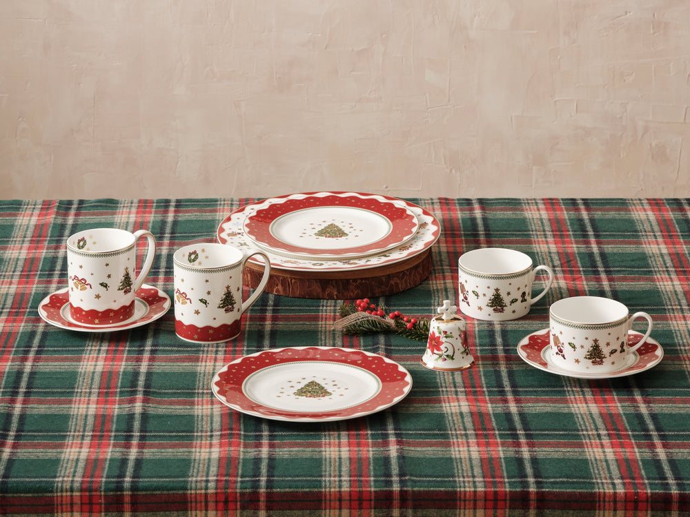My Noel holiday table setting showing plates, mugs, and a small Christmas bell on a green and red plaid tablecloth