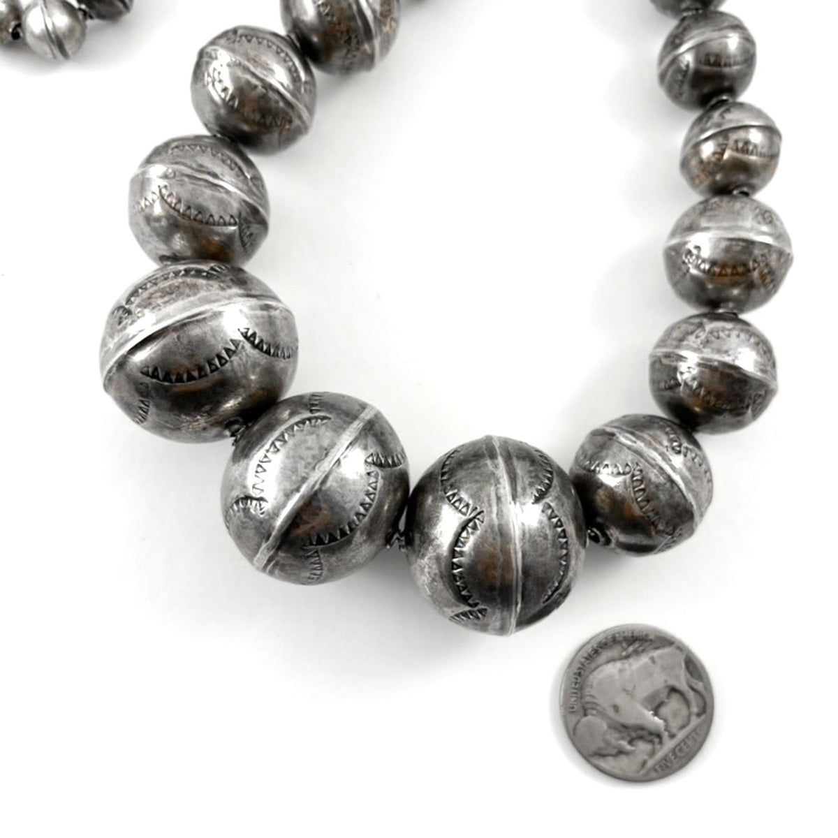 Close-up of handmade stamped silver beads showcasing graduated sizes with a coin for scale on a white background