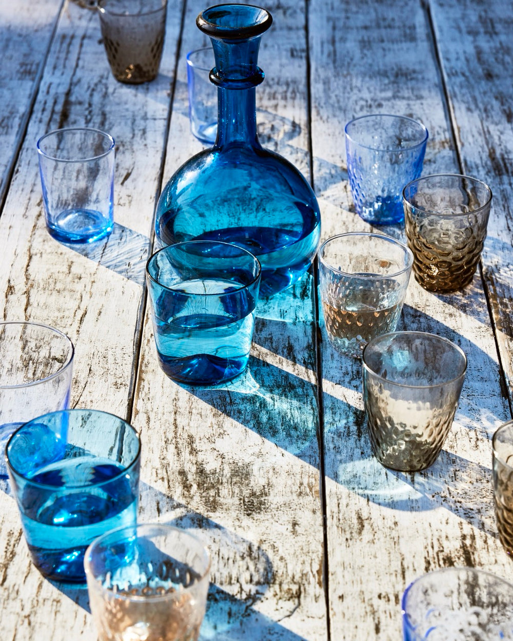 Front of Pienza Graduated Decanter, blue glass with rounded body and subtle gradation, with tumblers on white wood table