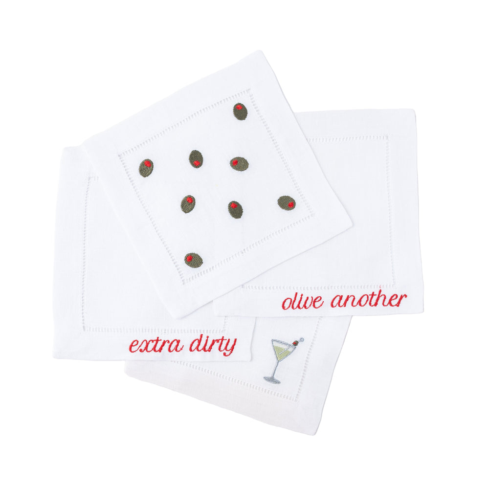 Overhead view of martini napkins set of 4 showing embroidered olives, martini glass, and red script on white linen