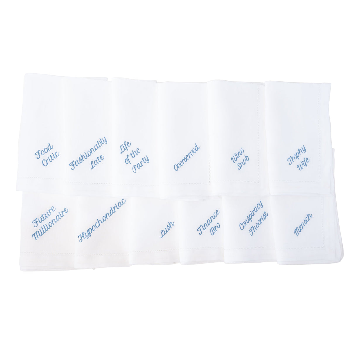Top view of Party Archetype dinner napkins showcasing blue embroidered personality titles on white linen background