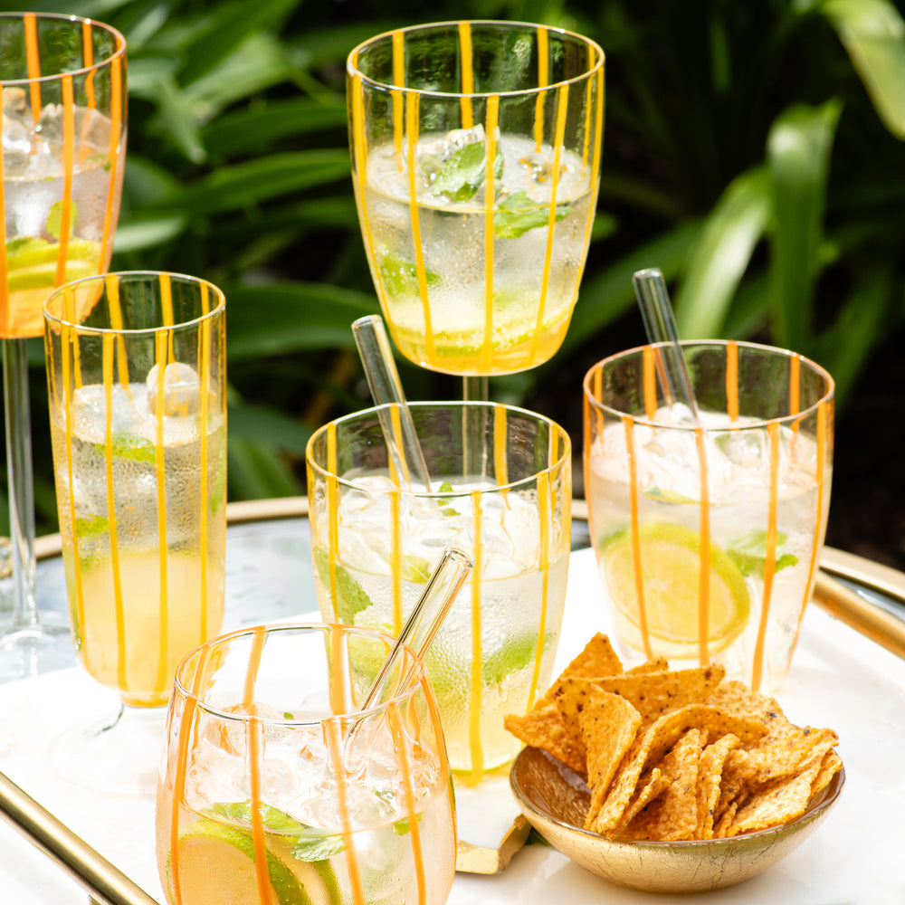 Angled view of Nuovo Stripe wine glass showing hand painted yellow vertical stripes on a tray with iced drinks and chips