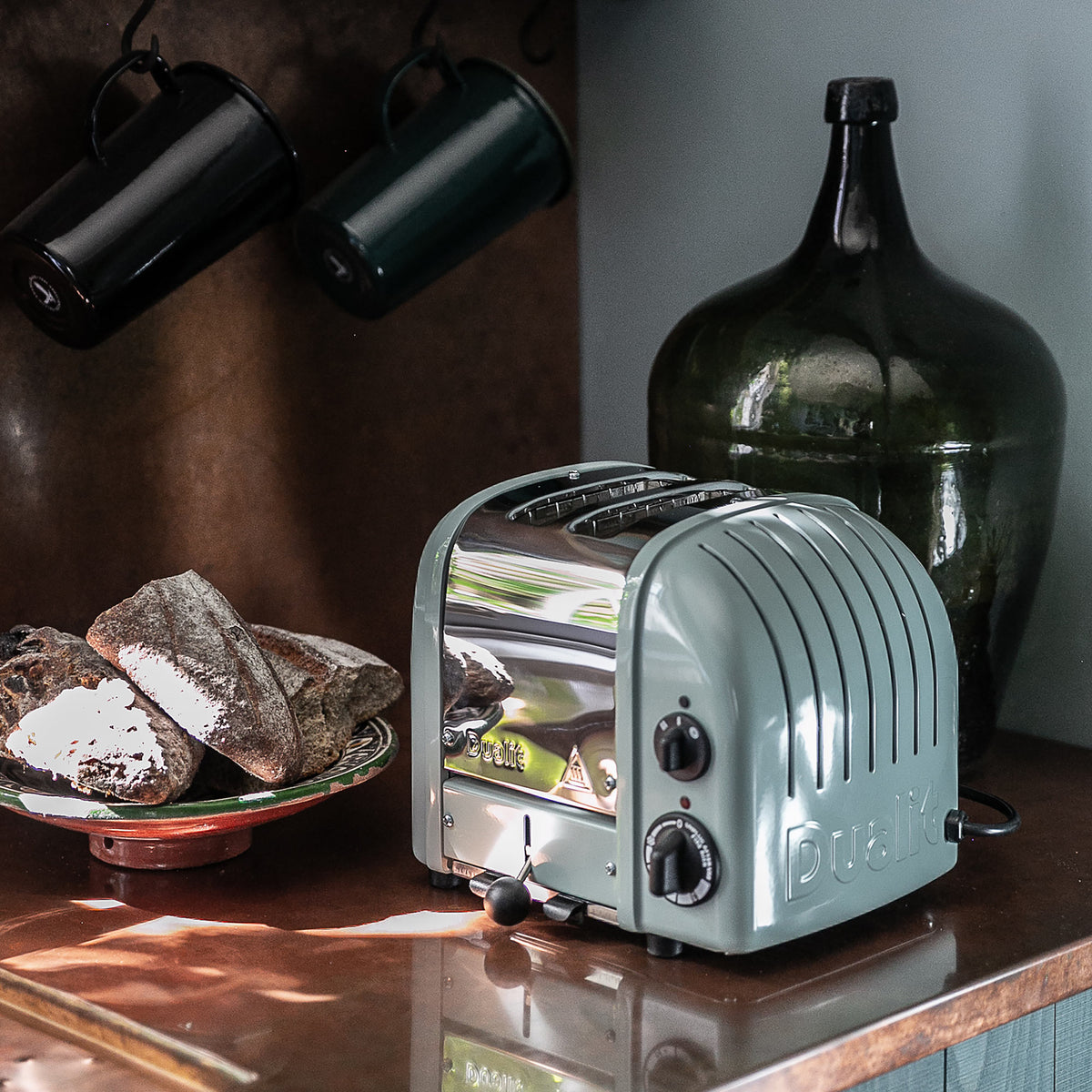 Three-quarter view of 2 Slot Classic Toaster in Eucalyptus with chrome front, two slots, and bread on a counter