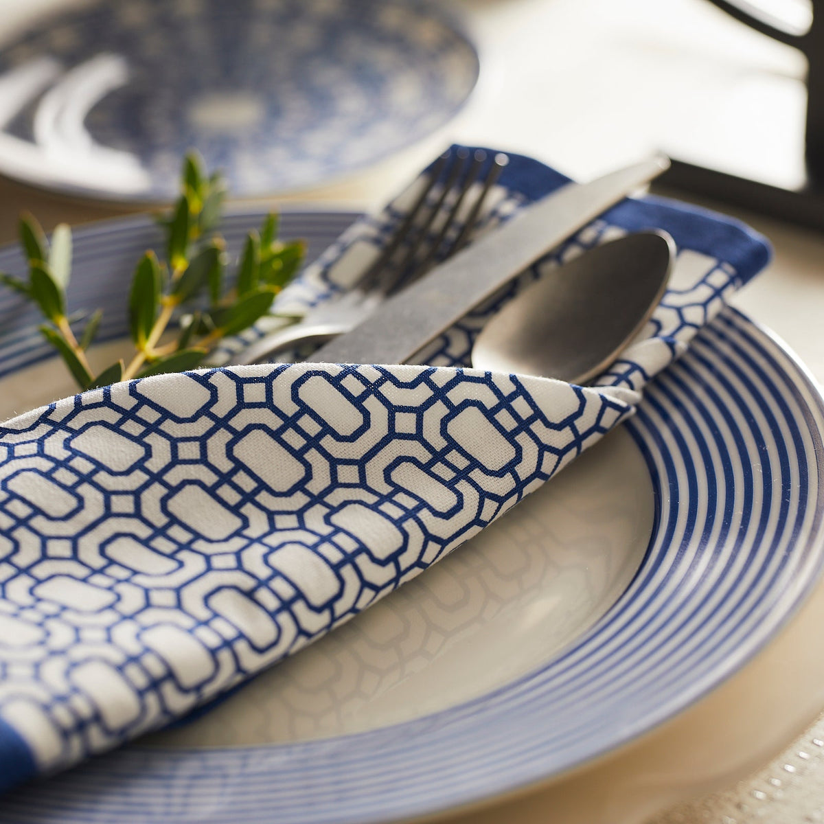 Blue patterned dinner napkin folded on a plate with coordinating blue tableware and silverware