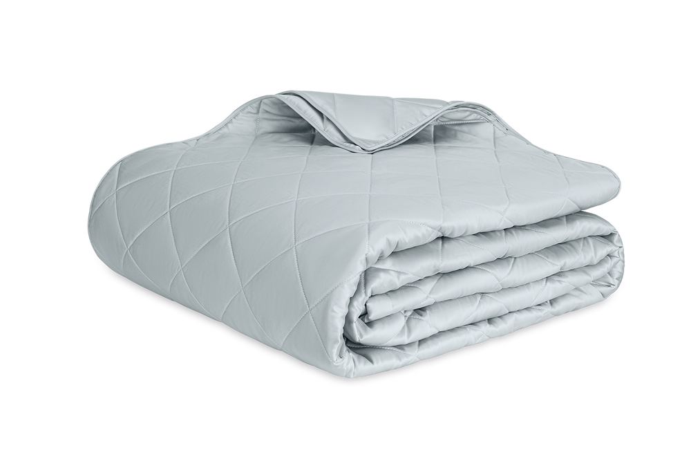 Angled view of Nocturne quilt folded to show diamond quilted pattern and stitched edges on white background