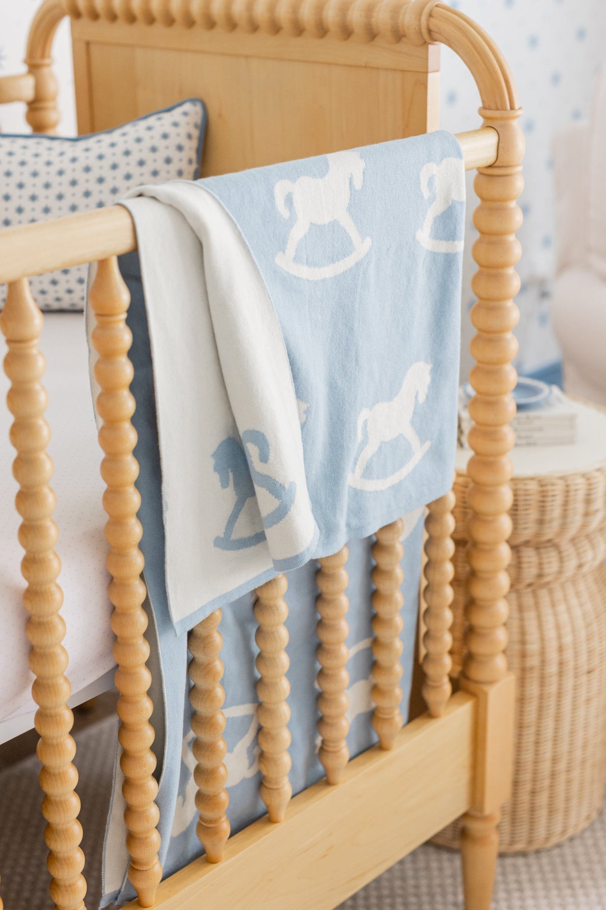 Draped view of Nursery Blanket in Blue Rocking Horse showcasing cream rocking horses on a light blue background with a wooden crib