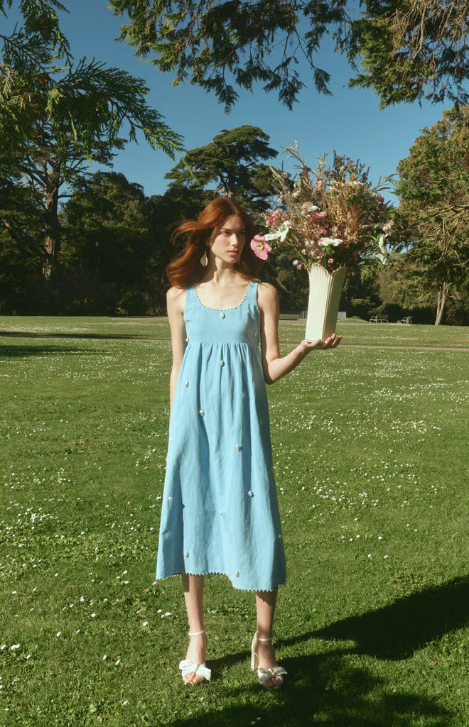 Front view of OTM Exclusive Emily Dress showcasing blue fabric with white pearl details and full skirt in a garden