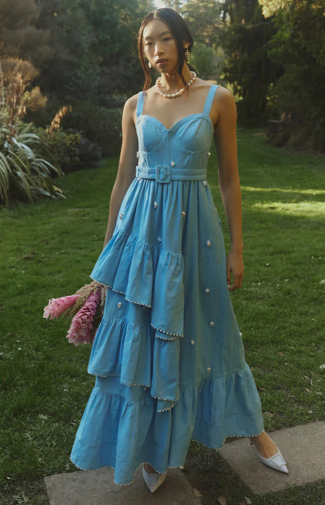 Front view of Reba Dress in blue with fitted sweetheart bodice, belted waist, tiered ruffle skirt and pearl accents outdoors