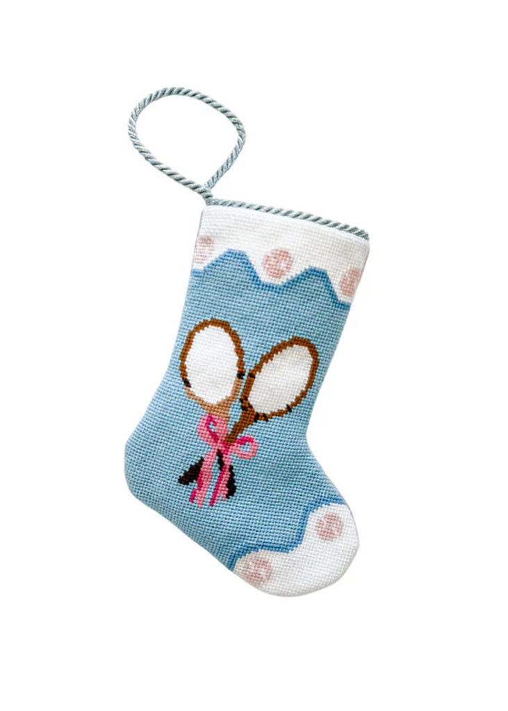 Front view of blue needlepoint Bauble stocking with stitched tennis racquets and pink bow, scalloped white cuff with pink dots, twisted hanging loop