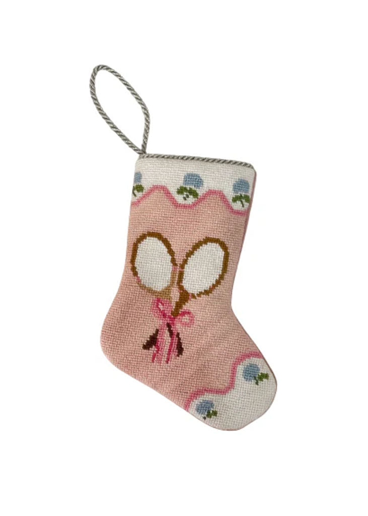 Front view of pink needlepoint stocking with crossed tennis rackets, scalloped white trim and silver loop on white background
