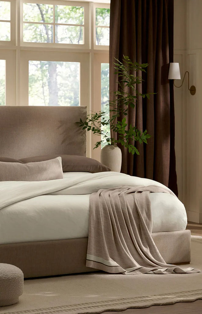 Draped over bed, Court Knit Throw Blanket in heathered oatmeal showcasing ribbed knit texture and finished border
