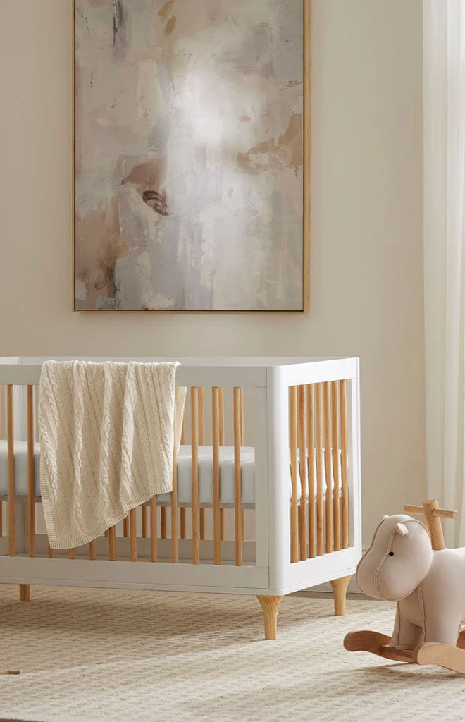 Natural cable knit baby blanket draped over white crib in a neutral nursery
