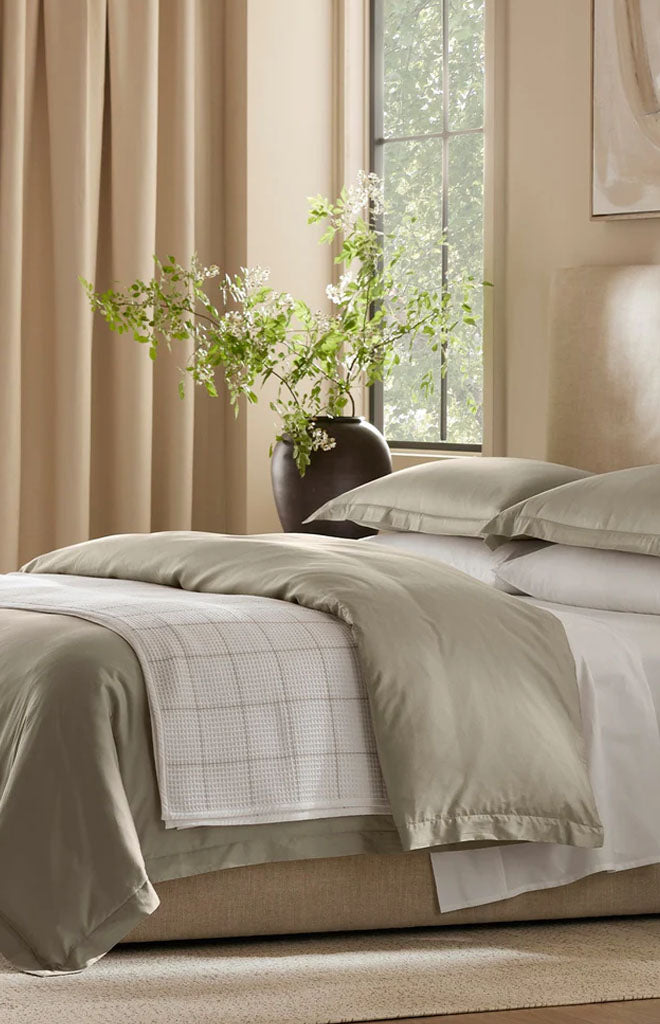 Angled view of Percale Hemmed Duvet Set in Oak showcasing layered bedding with pillows in a sunlit bedroom