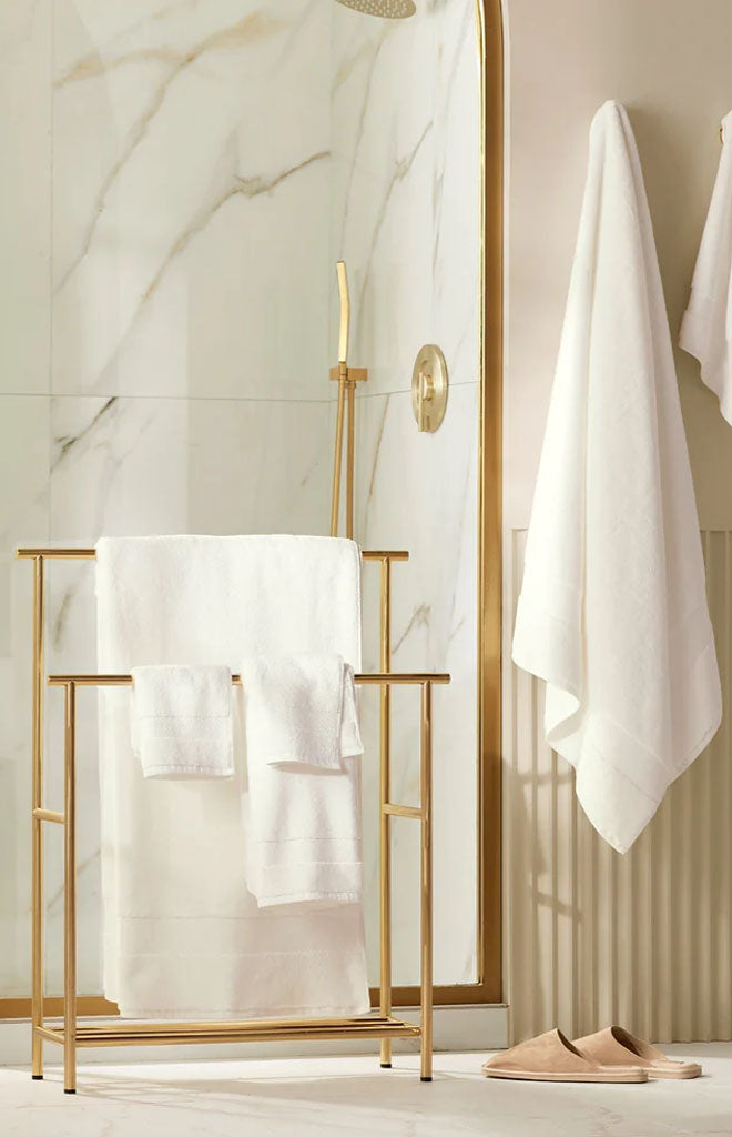 Front view of plush bath sheet set in white showcasing plush terry texture on a gold towel rack in a marble shower