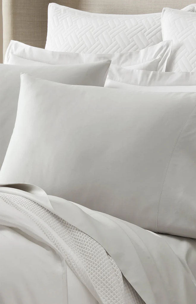 Close-up view of Percale Hemmed Pillowcase Set in Mist showcasing the 7-inch hemline with layered bedding background