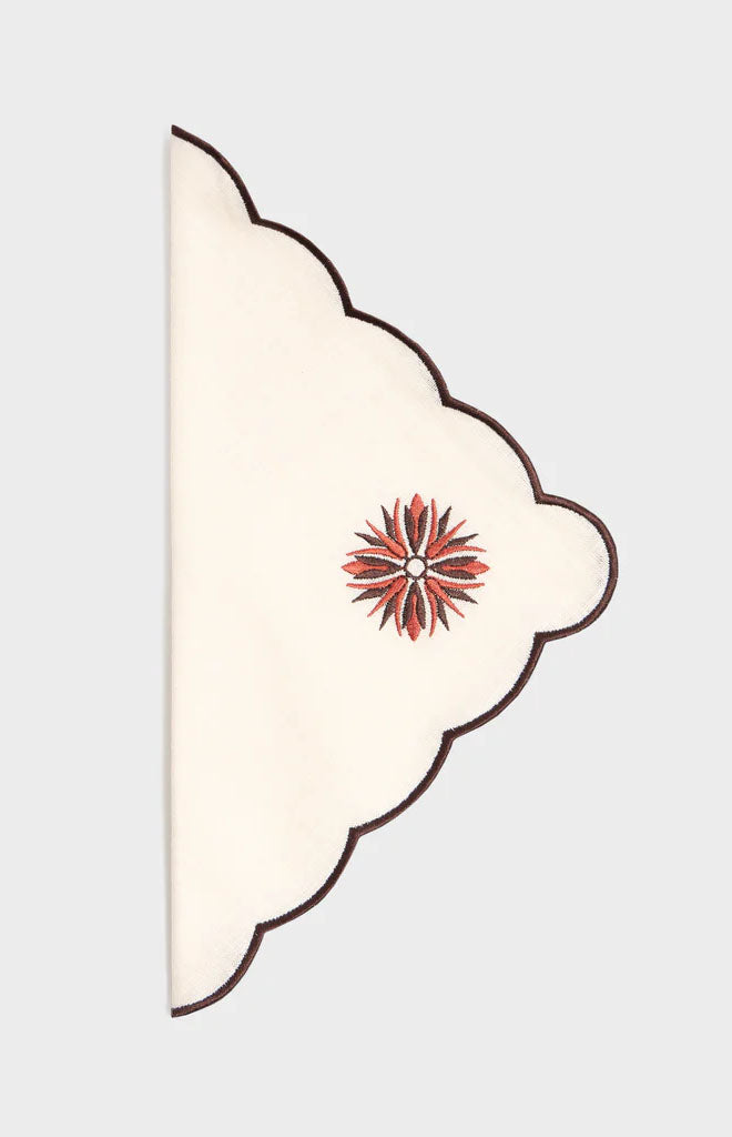 Folded Botanica Embroidered Napkin Terracotta in White/Burgundy with scalloped edges and floral medallion on gray
