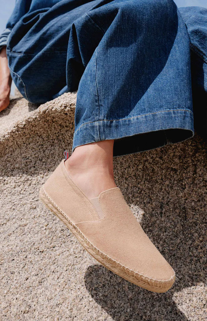 Side view of Men’s Joel 2 Espadrille in Sand Cotton showcasing slip-on design and jute sole with textured stone background