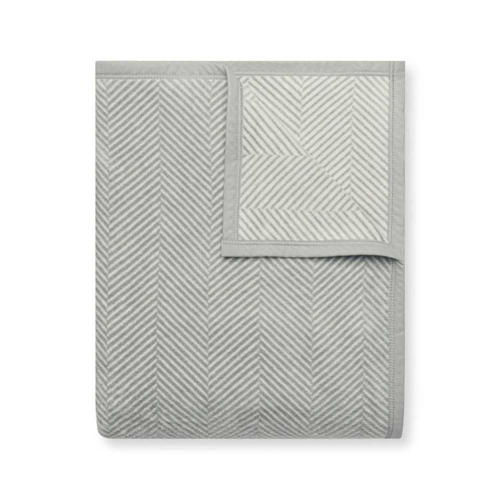 Folded Harborview Herringbone light grey blanket showing herringbone jacquard pattern and piped edge on white