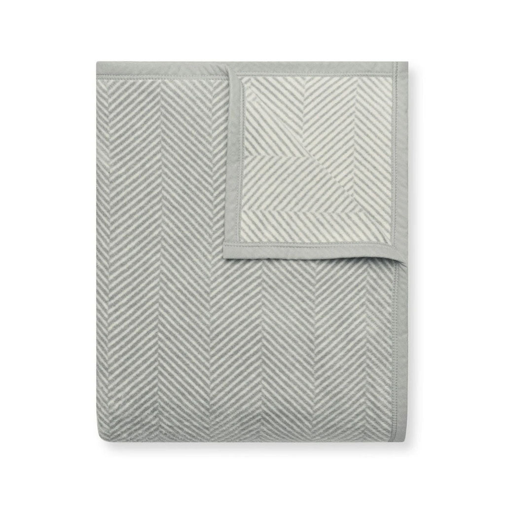 Folded Harborview Herringbone light grey blanket showing herringbone jacquard pattern and piped edge on white