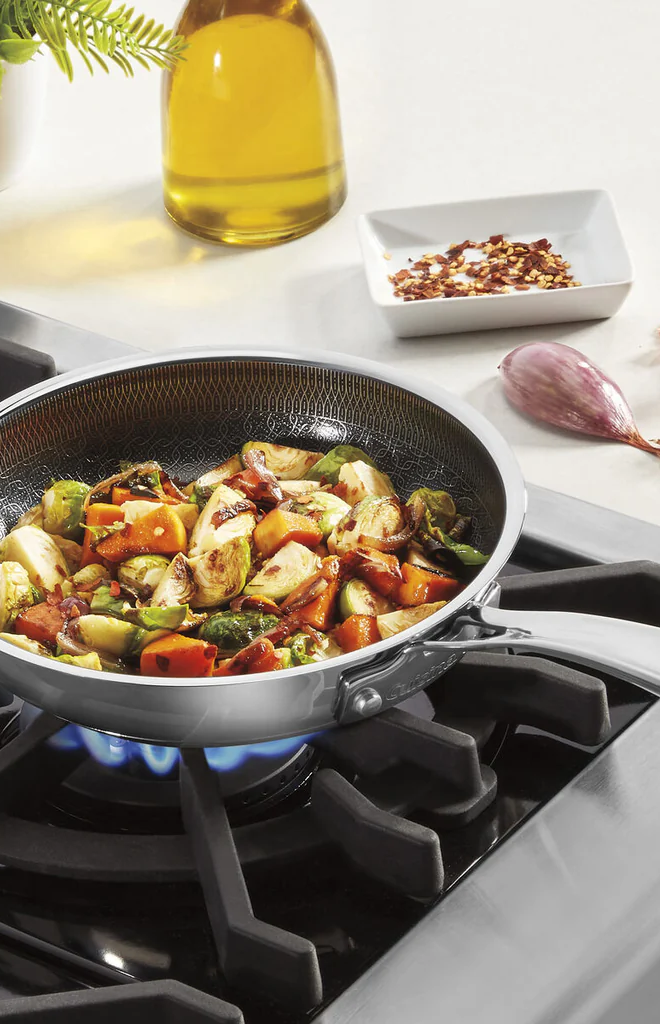 Cuisinart FusionPlus 8-inch stainless steel skillet sautéing vegetables on a gas stove with oil and spices nearby