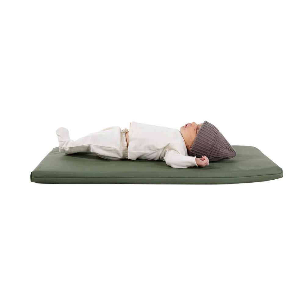 Side view of Padded Changing Mat in thyme showing cushioned memory-foam surface with a baby lying on a white background