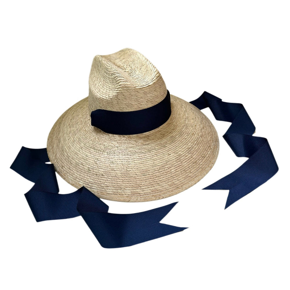 Angled top view of Hollyhock Sun Hat showcasing wide woven palm brim and long navy grosgrain ribbon on white background