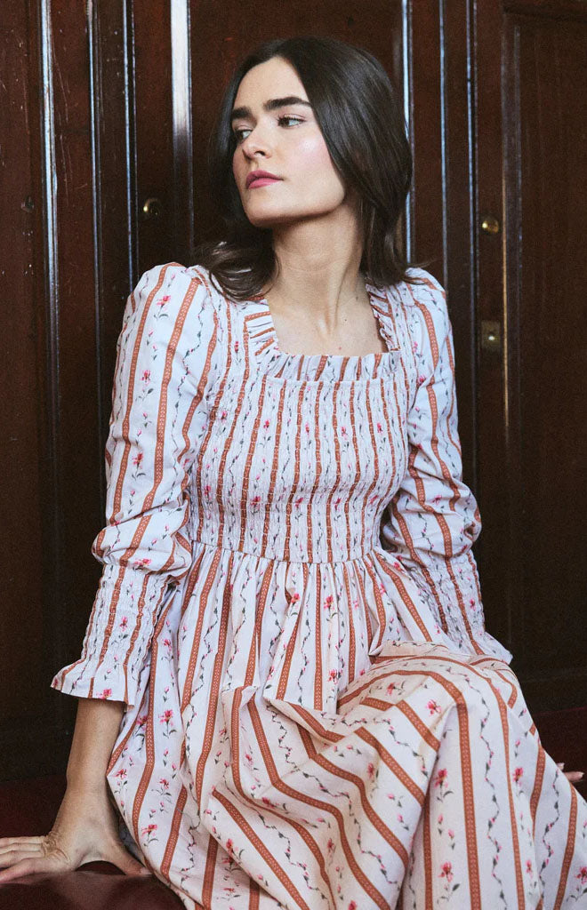 Seated three-quarter view of Eloise dress in Cherie with smocked bodice, ruffled square neckline, puff sleeves, floral